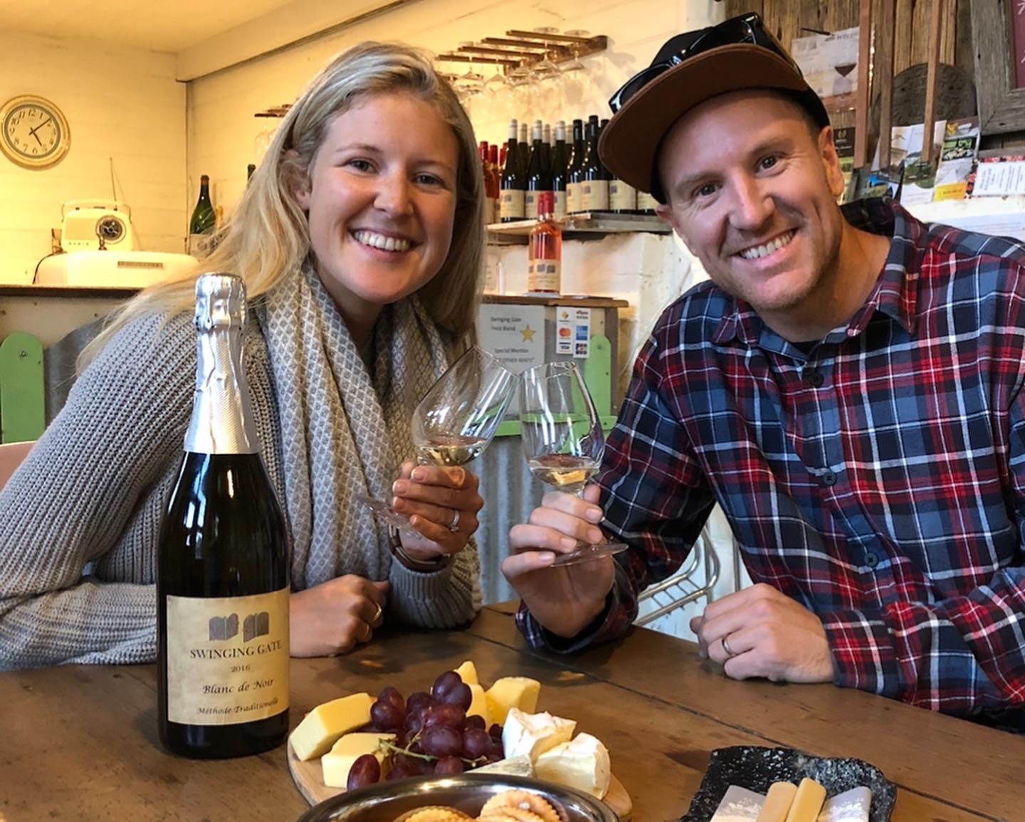 Two people smiling with wine glasses at a table with cheese and grapes.